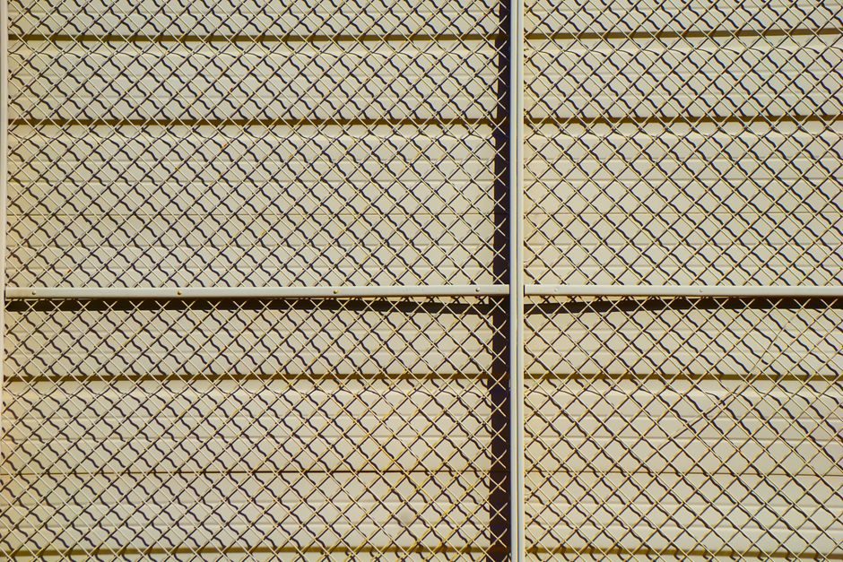 琬琰 — Detailed pattern of a chain-link fence casting shadows, creating a textured grid effect.
