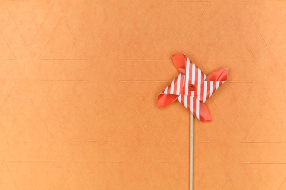 骍刚 — Minimalistic paper pinwheel with stripes against a textured orange backdrop, offering ample copy space.